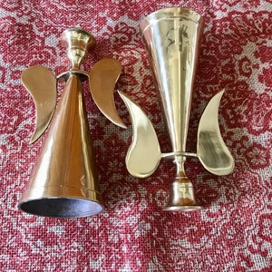 May include: Two gold metal angel candle holders. One is a cone shape with wings and the other is a trumpet shape with wings.