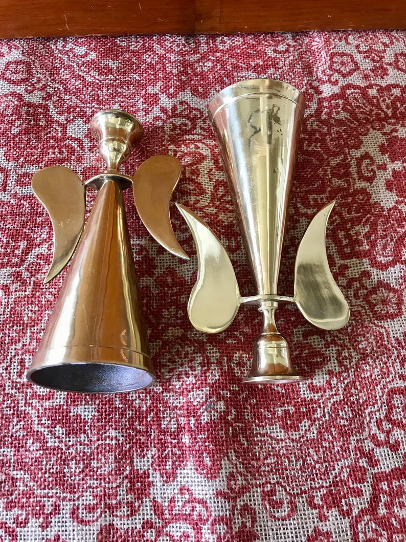 May include: Two gold metal angel candle holders. One is a cone shape with wings and the other is a trumpet shape with wings.