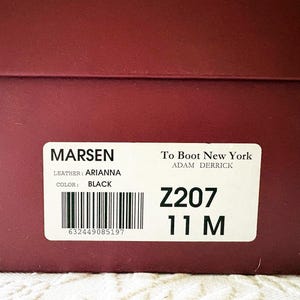 Puede incluir: Primer plano de una caja de zapatos granate con una etiqueta blanca. La etiqueta dice "MARSEN" y "To Boot New York". Los zapatos son negros, talla 11 M. La piel es "ARIANNA".