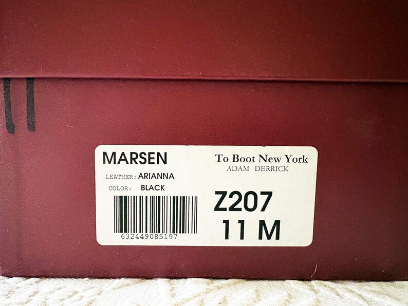 Puede incluir: Primer plano de una caja de zapatos granate con una etiqueta blanca. La etiqueta dice "MARSEN" y "To Boot New York". Los zapatos son negros, talla 11 M. La piel es "ARIANNA".