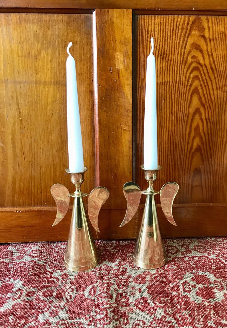 May include: Two gold angel candle holders with white candles. The candle holders have wings and a conical base.