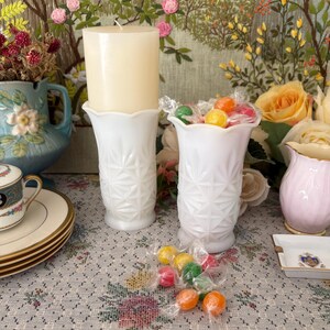 Pu&ograve; includere: Due vasi in vetro opalino bianco con un motivo a stella pressato e bordi smerlati. Un vaso contiene una candela a colonna color crema, mentre l'altro &egrave; riempito con caramelle colorate assortite avvolte in plastica trasparente.