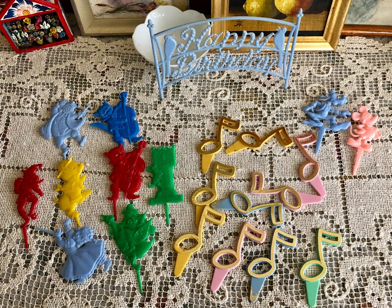 May include: A set of colorful plastic cake toppers featuring musical notes, characters from the Wizard of Oz, and a Mickey Mouse figure. The toppers are perfect for a birthday party or other celebration.