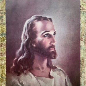 May include: A vintage print of a painting depicting a man with long brown hair and a beard. He is wearing a white robe and looking to the right. The background is a soft purple.