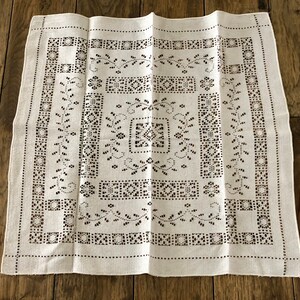 Peut inclure: Nappe en lin blanc avec un motif d&eacute;licat et complexe de petits carr&eacute;s et de motifs floraux. Le motif est cr&eacute;&eacute; par des d&eacute;coupes dans le tissu, cr&eacute;ant un effet de dentelle.