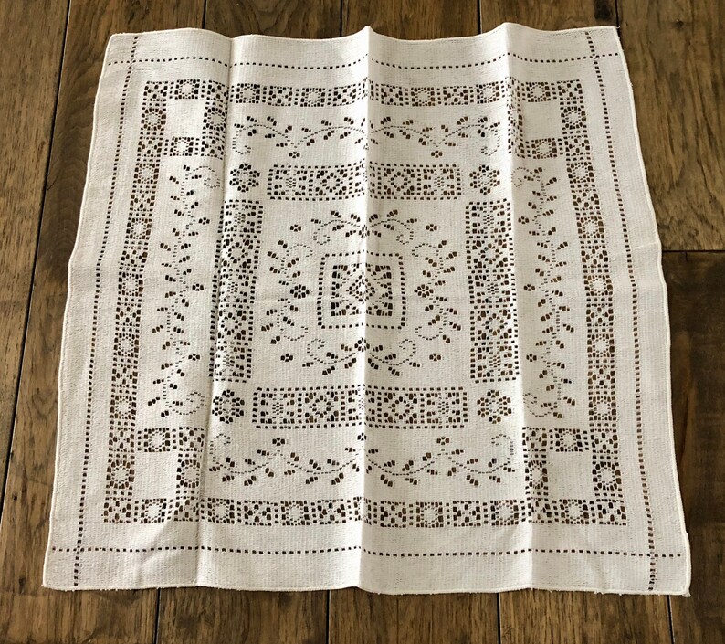 Peut inclure: Nappe en lin blanc avec un motif d&eacute;licat et complexe de petits carr&eacute;s et de motifs floraux. Le motif est cr&eacute;&eacute; par des d&eacute;coupes dans le tissu, cr&eacute;ant un effet de dentelle.