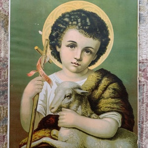 May include: A vintage religious print featuring a young boy with curly brown hair holding a white lamb. He is wearing a brown fur-trimmed robe and holding a wooden staff with a banner that reads "Ecce Agnus Dei". The background is a green and gold color.