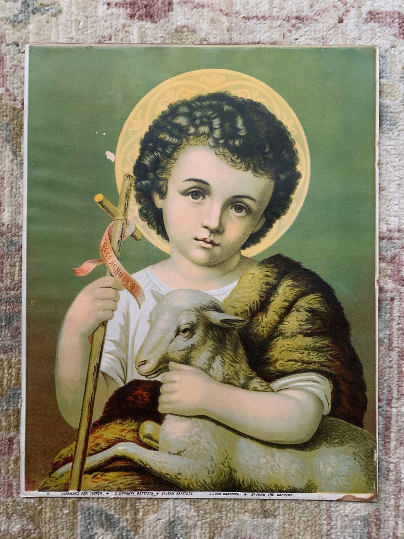 May include: A vintage religious print featuring a young boy with curly brown hair holding a white lamb. He is wearing a brown fur-trimmed robe and holding a wooden staff with a banner that reads "Ecce Agnus Dei". The background is a green and gold color.
