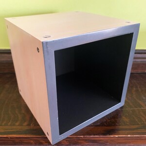 May include: A wooden cube storage box with a gray trim. The box is empty and has a black interior.