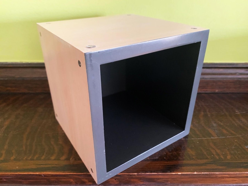 May include: A wooden cube storage box with a gray trim. The box is empty and has a black interior.