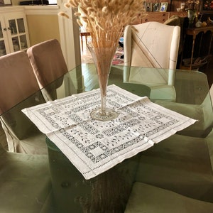 Peut inclure: Une table en verre avec une nappe blanche et un vase de pampas s&eacute;ch&eacute;es au centre. La table est entour&eacute;e de chaises avec des coussins beiges.