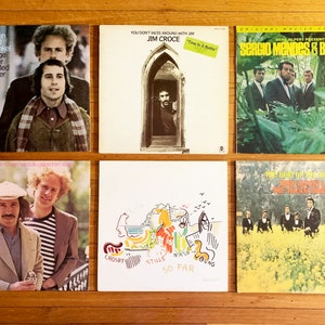 May include: Six vintage vinyl record album covers. The albums are by Simon and Garfunkel, Jim Croce, Sergio Mendes & Brasil '66, Crosby, Stills & Nash, and The Brass. The covers are all different colors and have different designs.