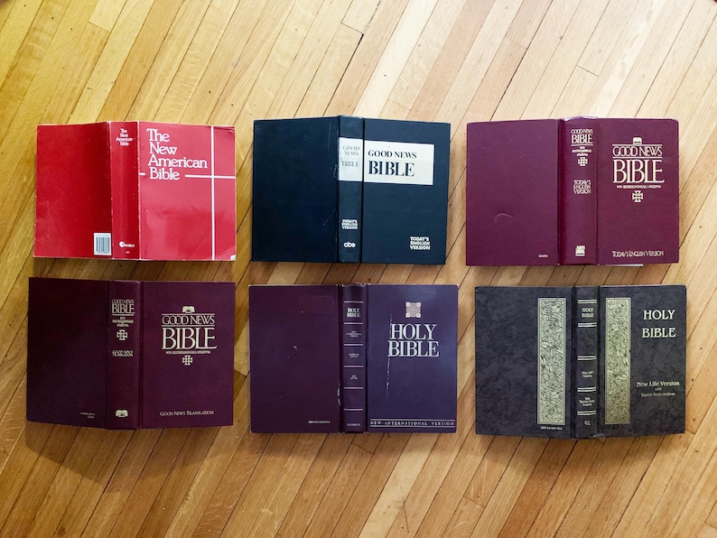 May include: A collection of eight different bible books, including The New American Bible, Good News Bible, and Holy Bible. The books are arranged in two rows of four, with the spines facing the viewer.