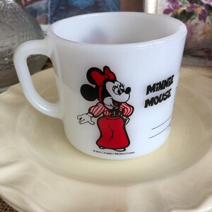 May include: White ceramic mug with a red and black image of Minnie Mouse wearing a red dress and white gloves. The text "Minnie Mouse" is printed in black on the mug. The copyright text "&copy; WALT DISNEY PRODUCTIONS" is printed in black at the bottom of the mug.