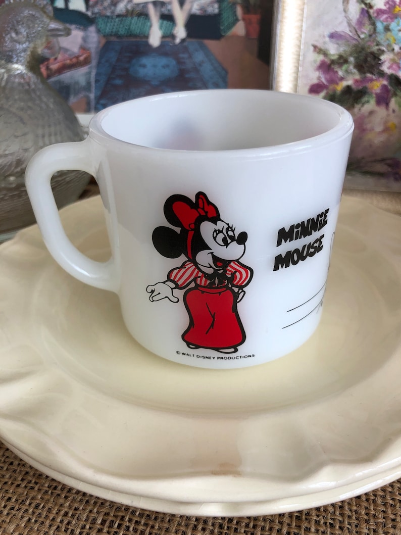 May include: White ceramic mug with a red and black image of Minnie Mouse wearing a red dress and white gloves. The text "Minnie Mouse" is printed in black on the mug. The copyright text "&copy; WALT DISNEY PRODUCTIONS" is printed in black at the bottom of the mug.