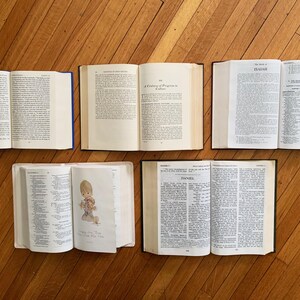 Op de afbeelding: Een luchtfoto van vijf open boeken op een houten oppervlak. De boeken hebben cr&egrave;mekleurige pagina's en zijn in een halve cirkel gerangschikt. De boekbanden zijn in verschillende kleuren, waaronder blauw en zwart. De boeken lijken religieuze teksten te zijn.