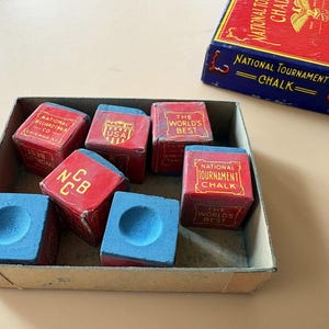 K&ouml;nnte beinhalten: Eine Sammlung roter und blauer Billardkreide-W&uuml;rfel in einer Pappschachtel, mit einer passenden Schachtel daneben. Die Kreidew&uuml;rfel haben eine blaue Kreideoberfl&auml;che und sind mit "National Tournament Chalk" und "The World's Best" beschriftet.