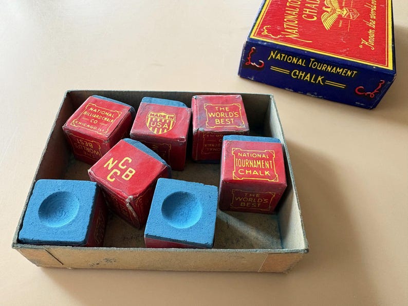 K&ouml;nnte beinhalten: Eine Sammlung roter und blauer Billardkreide-W&uuml;rfel in einer Pappschachtel, mit einer passenden Schachtel daneben. Die Kreidew&uuml;rfel haben eine blaue Kreideoberfl&auml;che und sind mit "National Tournament Chalk" und "The World's Best" beschriftet.