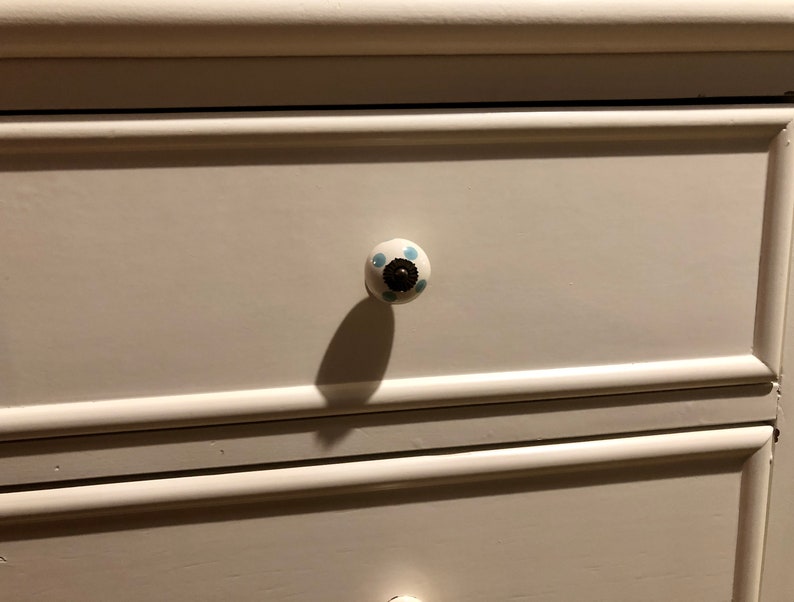 Puede incluir: C&oacute;moda blanca con dos cajones. El caj&oacute;n superior tiene un pomo de cer&aacute;mica blanca con lunares azules.