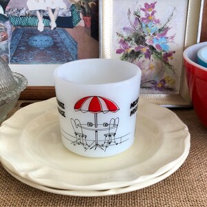 May include: White ceramic mug with a black and red illustration of a red and white striped umbrella, two chairs, and a table. The mug says "Nostalgia Village" on the side.