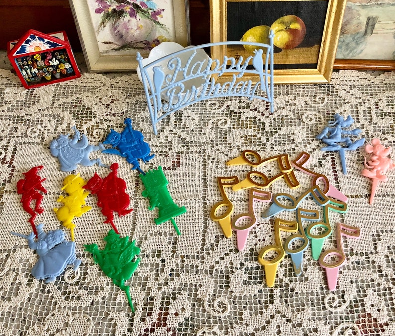 May include: A set of colorful plastic cake toppers featuring musical notes, a whimsical bridge with the words "Happy Birthday", and various characters. The toppers are perfect for adding a festive touch to a birthday cake.