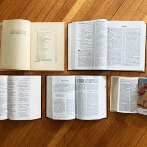 Op de afbeelding: Een bovenaanzicht van verschillende open boeken op een houten oppervlak. De boeken vari&euml;ren in grootte en inhoud, met tekst en illustraties. De pagina's zijn cr&egrave;mekleurig en de kaften zwart of wit.