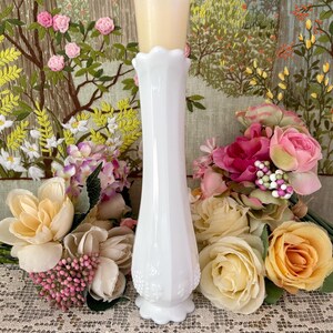 Peut inclure: Un vase blanc de style vintage avec un bord festonn&eacute; et une base d&eacute;corative. Une bougie beige est pos&eacute;e sur le vase. Le vase est entour&eacute; de bouquets de fleurs roses, jaunes et cr&egrave;me, sur une tapisserie florale.