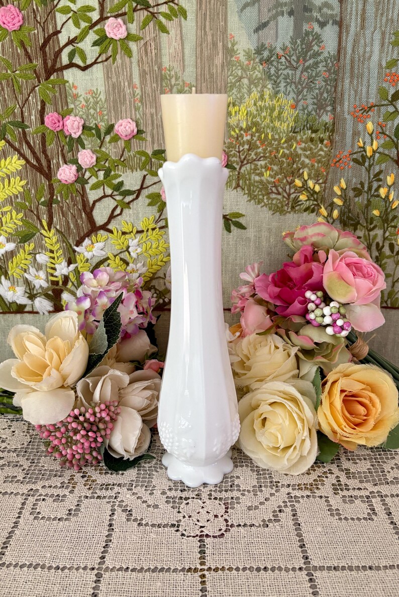 Peut inclure: Un vase blanc de style vintage avec un bord festonn&eacute; et une base d&eacute;corative. Une bougie beige est pos&eacute;e sur le vase. Le vase est entour&eacute; de bouquets de fleurs roses, jaunes et cr&egrave;me, sur une tapisserie florale.
