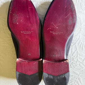 Puede incluir: Un par de zapatos de vestir negros con suelas burdeos. Las suelas est&aacute;n marcadas con el texto "To Boot New York" y la talla "11". Los zapatos tienen un dise&ntilde;o cl&aacute;sico.