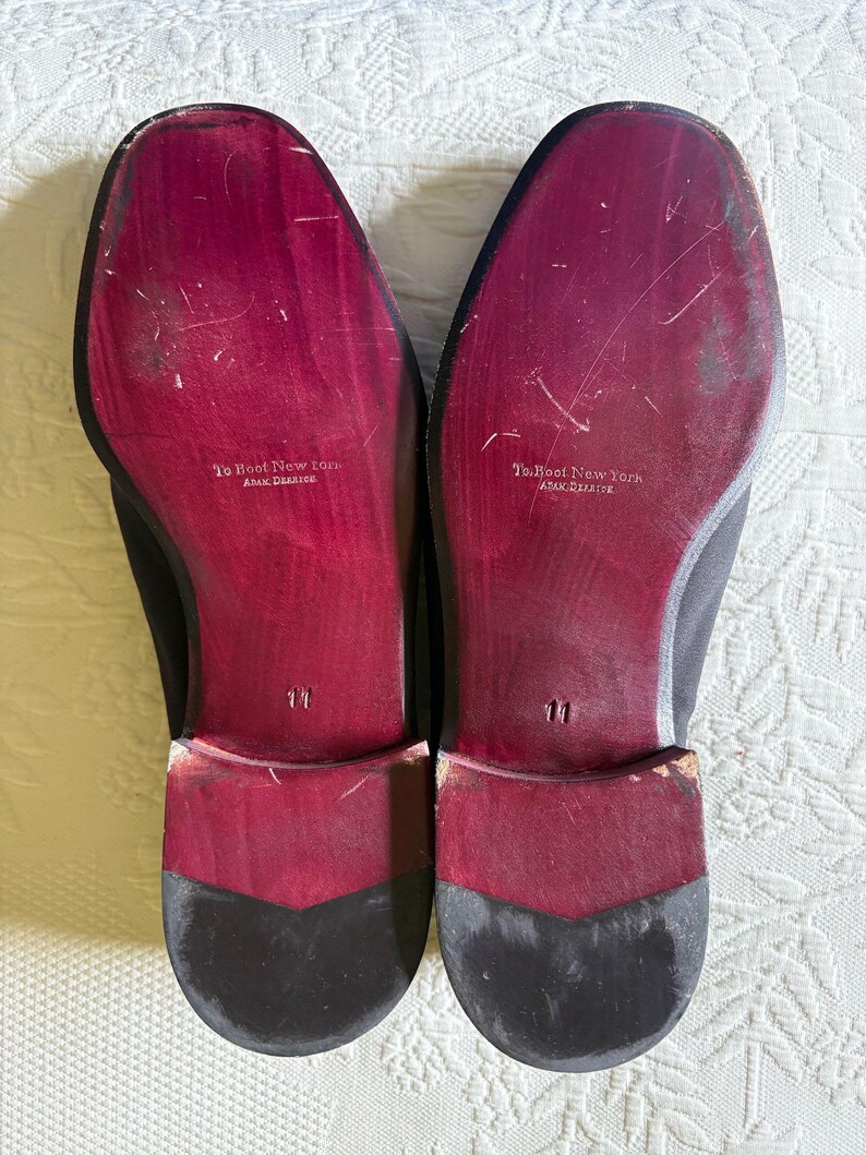 Puede incluir: Un par de zapatos de vestir negros con suelas burdeos. Las suelas est&aacute;n marcadas con el texto "To Boot New York" y la talla "11". Los zapatos tienen un dise&ntilde;o cl&aacute;sico.