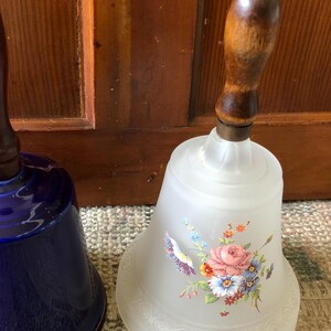 May include: Two decorative glass bells with wooden handles. One bell is frosted glass with a floral design and the other is a deep blue color.
