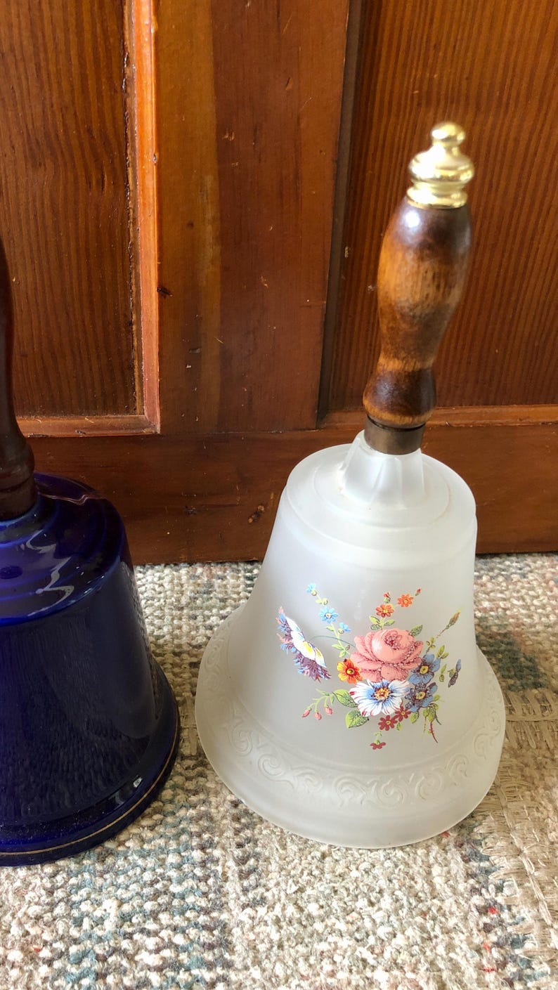 May include: Two decorative glass bells with wooden handles. One bell is frosted glass with a floral design and the other is a deep blue color.