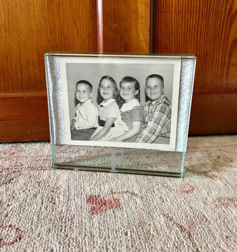 May include: A black and white photo of four children in a glass picture frame with a decorative border. The frame is sitting on a white rug with a pink floral pattern.