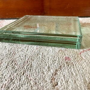 May include: A clear glass square tray with two layers. The tray is sitting on a white carpet with pink accents.