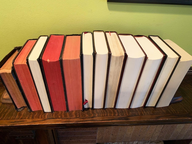 May include: A row of ten hardback books with red and white spines. The books are arranged in a line on a wooden surface.