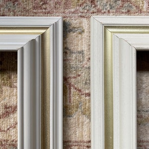 May include: Two white picture frames with gold trim. The frames are side by side and are both in focus.
