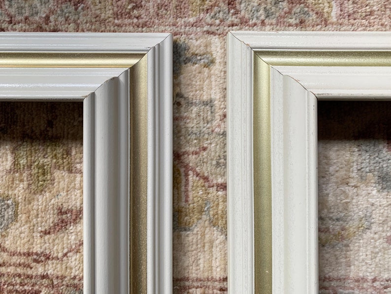 May include: Two white picture frames with gold trim. The frames are side by side and are both in focus.