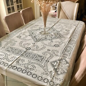Peut inclure: Une nappe blanche avec un motif de dentelle noire, dress&eacute;e pour un d&icirc;ner. Un vase avec des fleurs s&eacute;ch&eacute;es beiges se trouve au centre de la table.