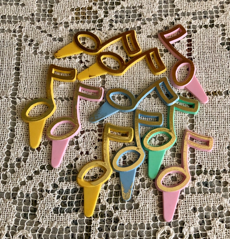 May include: A set of nine colorful plastic musical note cake toppers. The notes are outlined in gold and have a vintage look. The colors include pink, yellow, blue, and green.