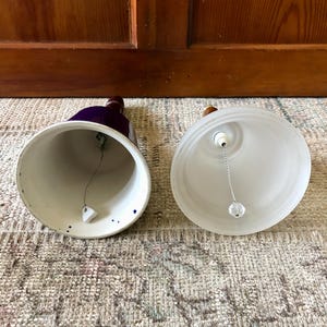 May include: Two ceramic bells, one with a blue and white glaze and the other with a frosted white glaze. Both bells have a wooden handle and a metal clapper.