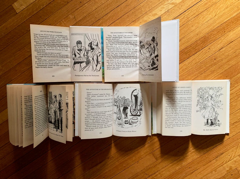 May include: A collection of vintage children's books with black and white illustrations. The books are open to different pages, showing various scenes and text. The books are on a wooden surface.