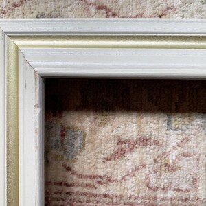 May include: A white picture frame with a gold trim. The frame is made of wood and has a simple design.