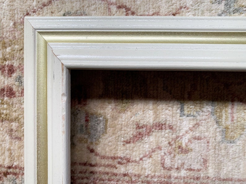 May include: A white picture frame with a gold trim. The frame is made of wood and has a simple design.