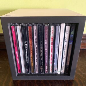 May include: A black CD storage unit with a variety of music CDs, including albums by The Animals, Neil Diamond, The Guess Who, The Hollies, Carole King, Gordon Lightfoot, Simon and Garfunkel, Cat Stevens, James Taylor, and more.