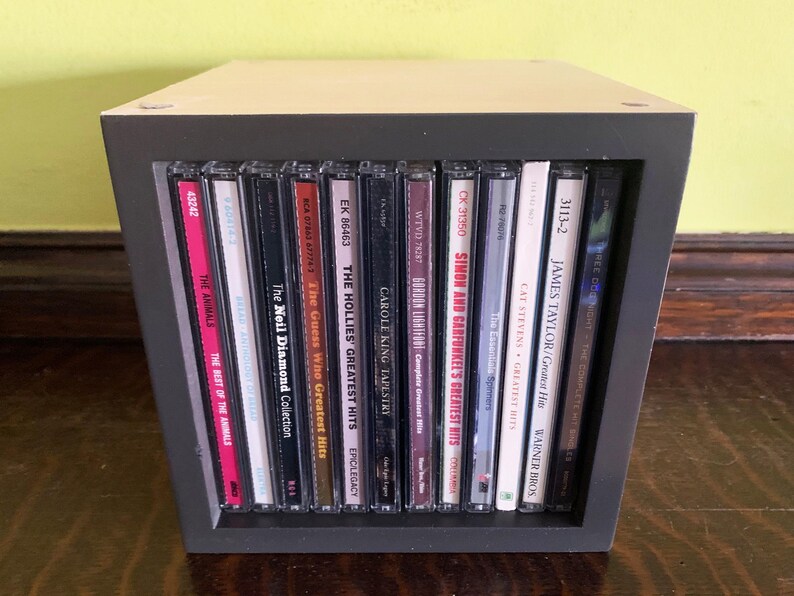 May include: A black CD storage unit with a variety of music CDs, including albums by The Animals, Neil Diamond, The Guess Who, The Hollies, Carole King, Gordon Lightfoot, Simon and Garfunkel, Cat Stevens, James Taylor, and more.