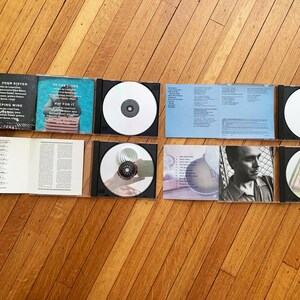 May include: A set of six CDs with accompanying booklets. The CDs are silver with various designs. The booklets are blue, white, and black with text. The text on the booklets includes the titles "Tell Your Sister", "Weeping Wine", "To The Lions", "Pay For It", and "The New Recordings".