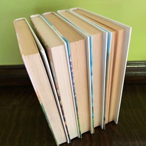 May include: A stack of six paperback books with white covers and colorful spines. The books are arranged vertically with the spines facing out.