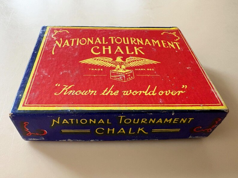 K&ouml;nnte beinhalten: Rechteckige Schachtel mit "National Tournament Chalk" mit roter Oberseite und blauen Seiten. Die Oberseite zeigt goldfarbene Schrift und ein Adleremblem. Der Text "Known the world over" ist ebenfalls sichtbar.