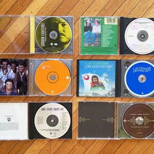 May include: A collection of ten vinyl records in clear plastic cases. The records are arranged in two rows of five. The records are all different colors and have different titles. The titles include "Gordon Lightfoot", "Cat Stevens Greatest Hits", "James Taylor's Greatest Hits", and "Three Dog Night".