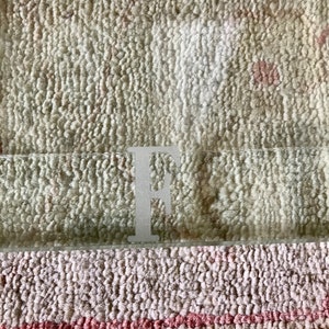 May include: A clear glass tray with the letter "F" etched on the bottom. The tray is sitting on a beige and pink patterned rug.